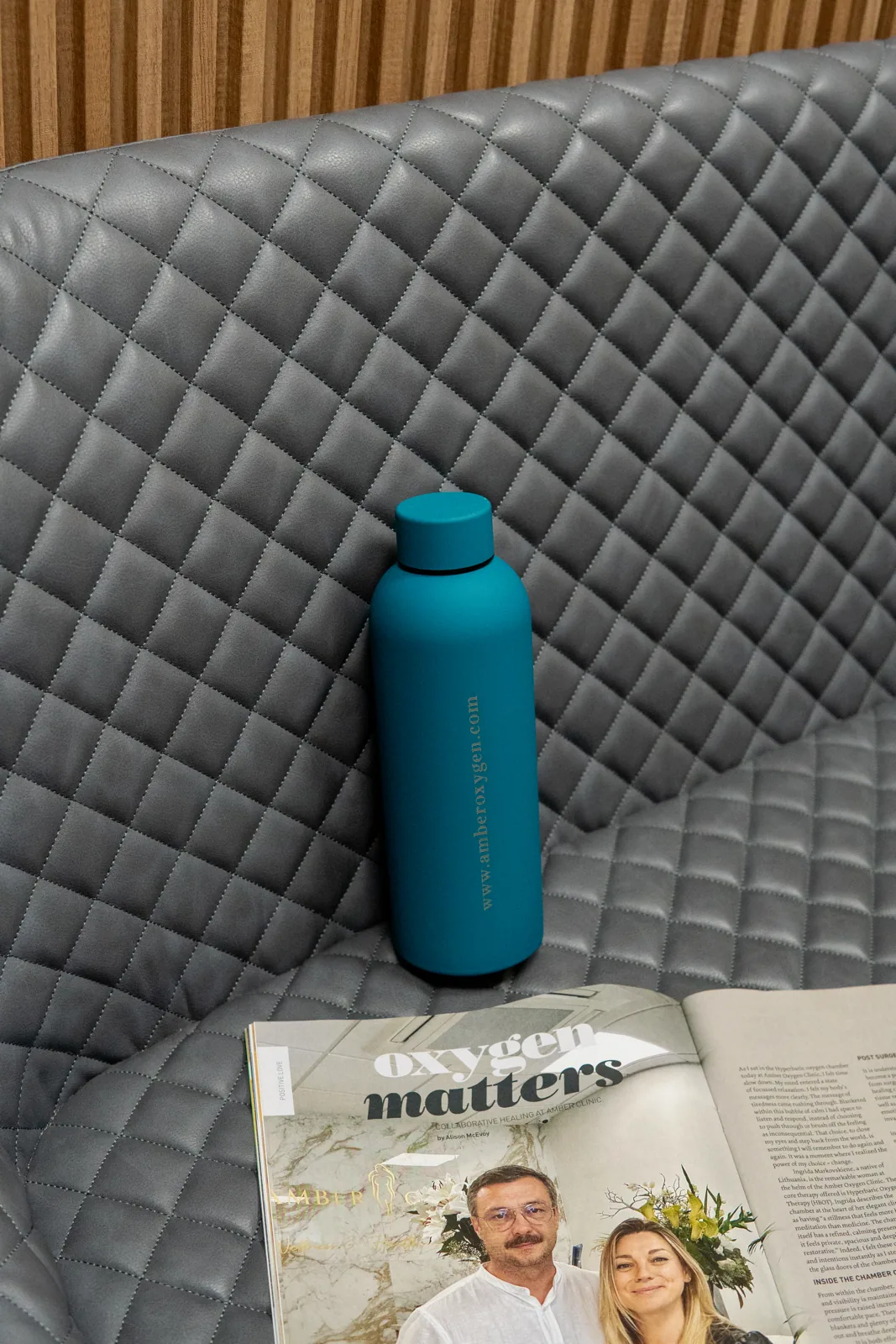 A turquoise bottle and an open magazine on a grey seat at Amber Oxygen
