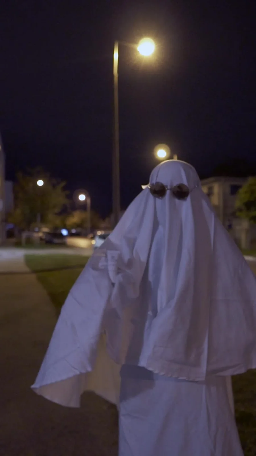 A ghost-like Halloween character wearing sunglasses on an evening street in Győr