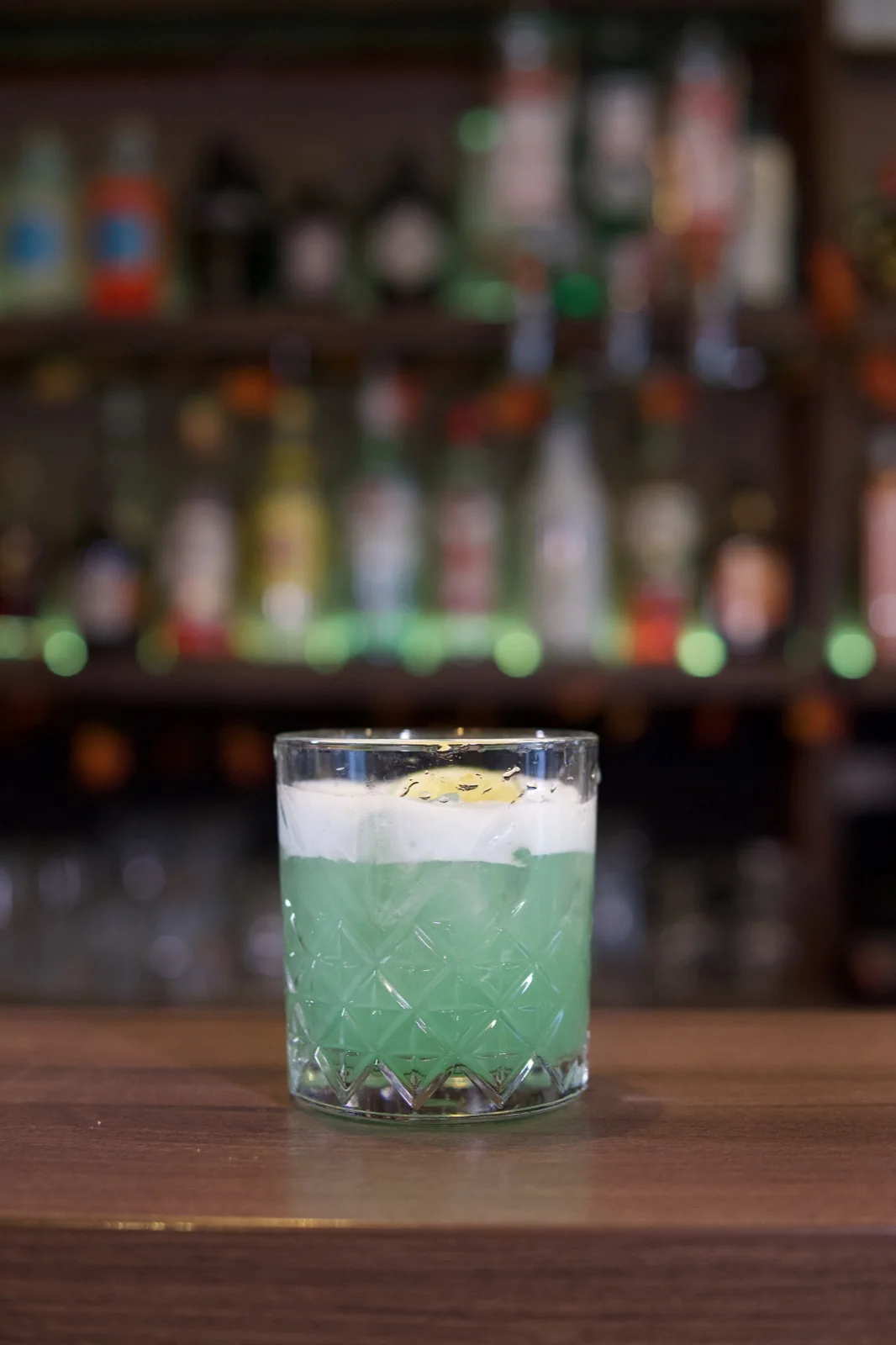A green drink with ice, citrus and a striped straw at Úri Muri