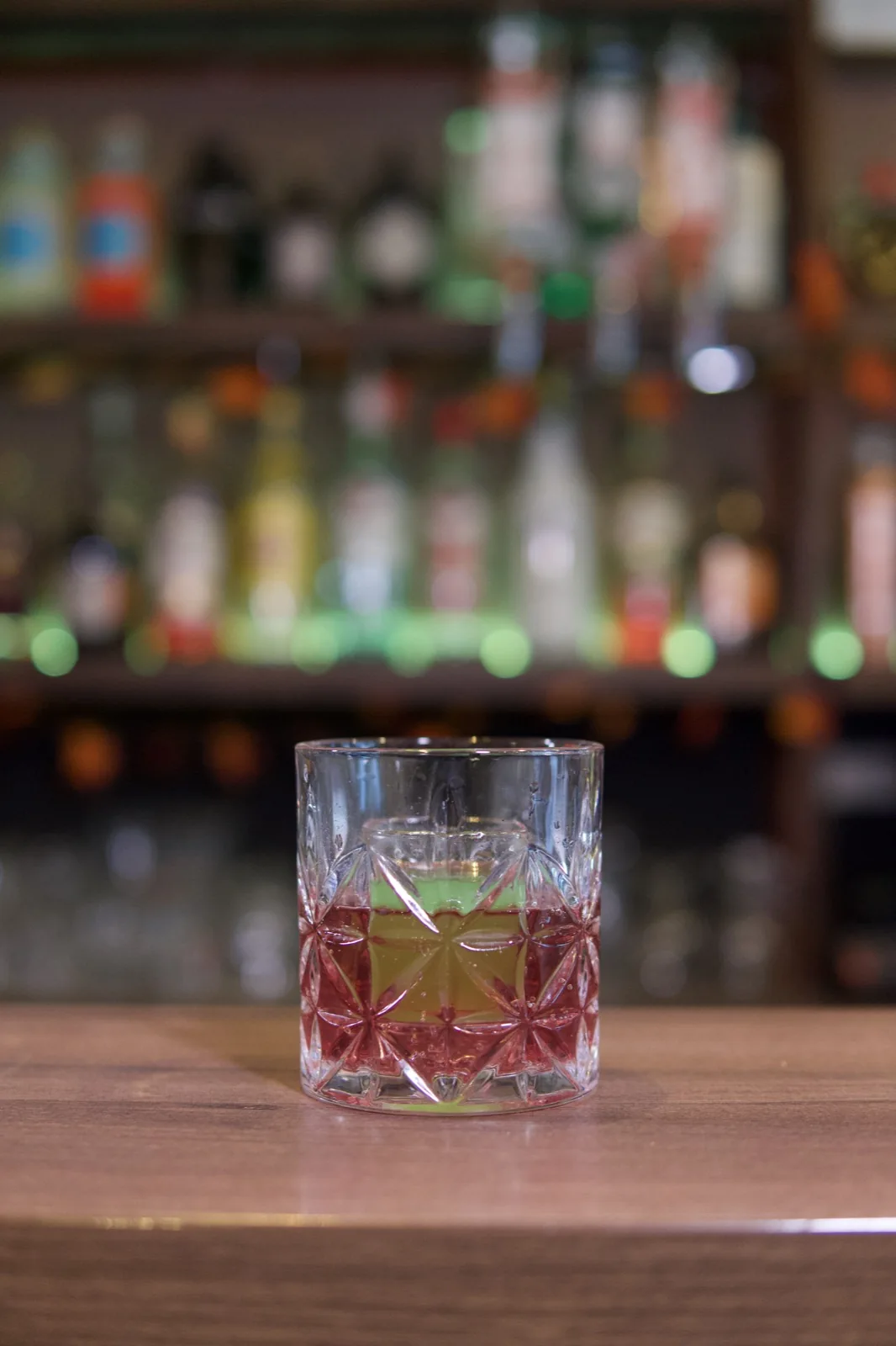 A red drink in a textured glass with the bar softly behind it